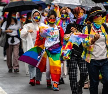 Das Bild zeigt mehrere Personen, mit Regenbogenfahnen und Schaals
