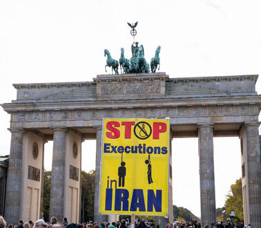 Vor dem Brandenburger Tor in Berlin demonstrieren Menschen, sie halten ein Plakat hoch auf dem geschrieben steht "Stop Executions Iran".