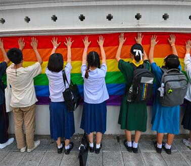 Das Bild zeigt mehrere Jugendliche, die eine Regenbogen-Fahne mit ihren Händen berühren
