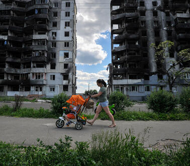 Eine Frau mit Kinderwagen vor zerstörten Hochhäusern