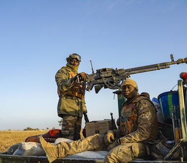 Das Foto zeigt zwei schwer bewaffnete Soldaten, die auf der Ladefläche eines Transporters sitzen und in die Kamera schauen.