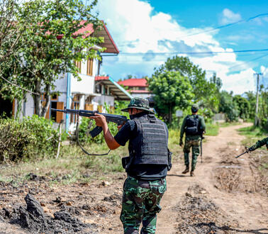 Drei Soldaten mit erhobenem Gewehr in einem Dorf