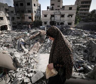 Eine Frau mit Kopftuch vor zerstörten Häusern