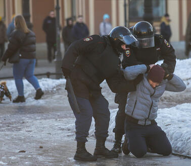Zwei Puniformierte Polizisten packen einen am Boden knieenden Mann.
