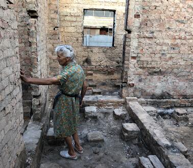 Das Bild zeigt eine ältere Frau in einer Hausruine