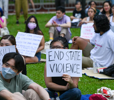 Junge Menschen sitzen auf dem Boden und halten Protestschilder in der Hand