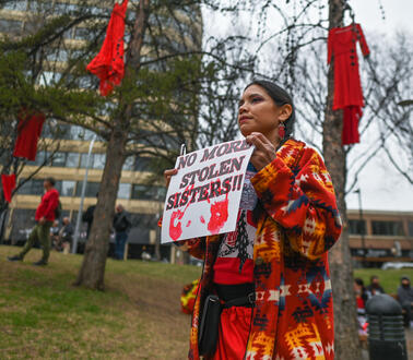 Eine Frau in traditioneller indigener Kleidung hält ein Schild mit der Aufschrift: „No more stolen sisters“