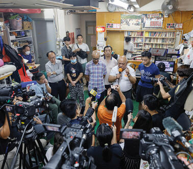 TV-Journalisten in einem Redaktionsraum, ein Mann steht an einem Mikrofon.