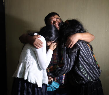 Das Bild zeigt einen Mann, der die Augen geschlossen hat, grinst und zwei Frauen umarmt.