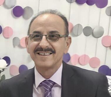 Porträtgoto von Bassem al-Zaak mit Brille und Schnäuzer. Er trägt einen Anzug und eine Krawatte und lächelt in die Kamera.