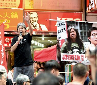 Das Foto zeigt Leung Kwok-hung, der bei einer Demonstration mit einem Mikrofon in der rechten Hand auf einer Bühene steht und zu der Menschenmenge spricht.