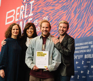 Gruppenfoto der drei Jury-Mitglieder und dem Regisseur, der eine Urkunde in der Hand hält. Die vier Personen stehen nebeneinander und lächeln.