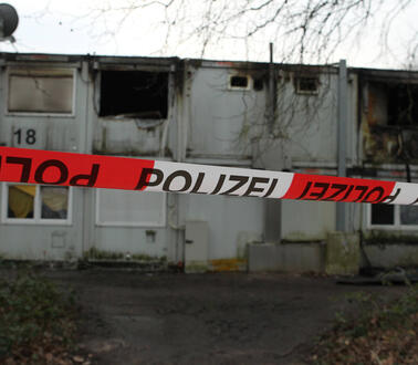 Wohncontainer, übereinandergestapelt, zum Teil ausgebrannt, abgesperrt mit einem Polizeiband.