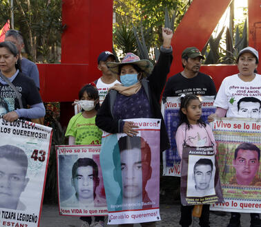 Das Foto zeigt mehrere Personen bei einer Demonstration, die Plakate mit Porträtfotos der entführten Studenten vor sich halten. Eine Frau in der Mitte des Fotos reckt ihre linke Faust in die Höhe.