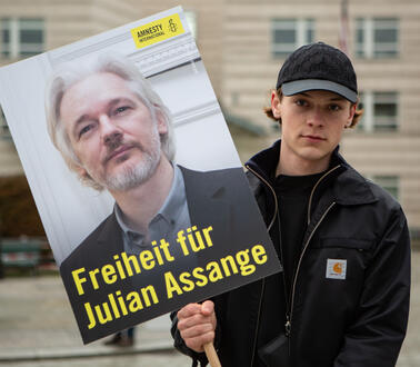 Das Bild zeigt einen jungen Mann mit einem Protestplakat "Freiheit für Julian Assange"