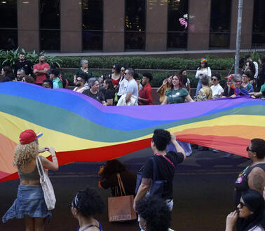 Das Bild zeigt Menschen, mit einen großen Regenbogenflagge
