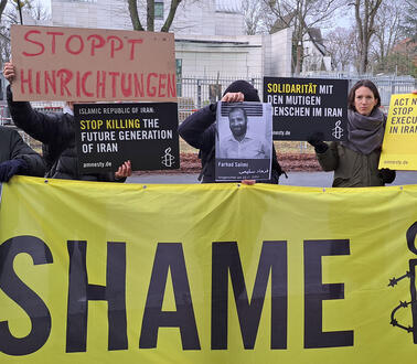 Das Bild zeigt mehrere Menschen mit Protestplakaten, eines mit dem Schriftzug "Shame"