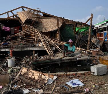 Das Bild zeigt eine Person, wie sie vor einem komplett zerstörten Haus sitzt