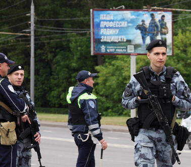 Das Foto zeigt vier wartende uniformierte Polizisten am Rande einer Straße. Zwei von ihnen sind mit Sturmgewehren bewaffent.