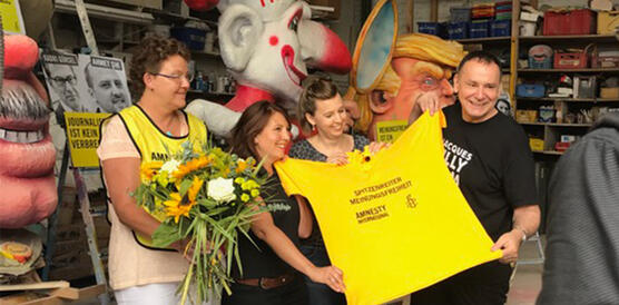 Lachende Menschen halten ein gelbes T-Shirt von Amnesty International in die Kamera