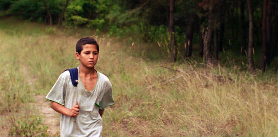 Ein Junge mit verschlissenem T-Shirt läuft über einen Feldweg am Waldrand