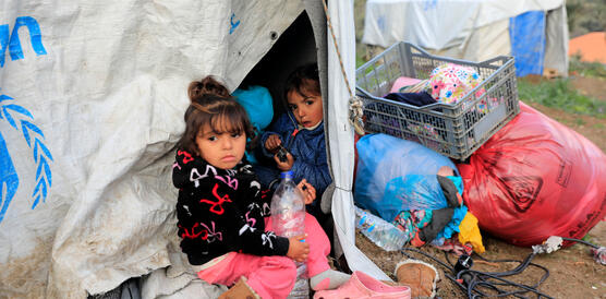 Zwei kleine Mädchen schauen aus einem Zelt, neben dem Plastiksäcke liegen