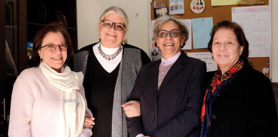 Vier lächelnde Frauen stehen in einem Büro vor einer Pinnwand 