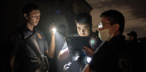 Drei philippinische Polizisten, einer leuchtet mit einer Taschenlampe, während ein anderer in eine Akte guckt