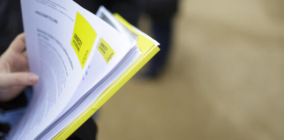 Aufnahme einer Hand, die mehrere Zettel mit Text und Amnesty-Logo und eine Pressemappe hält