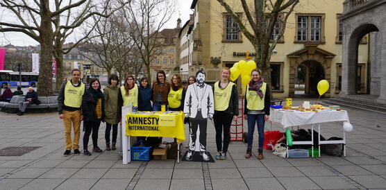 Eine Gruppe junger Menschen steht hinter einem Amnesty-Stand mit Luftballons und Kuchen