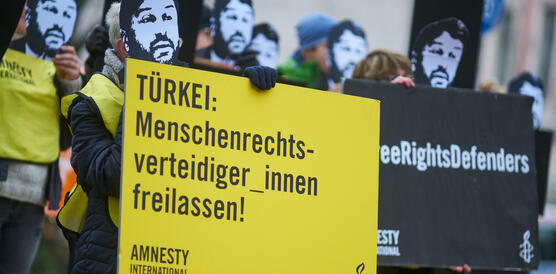 Eine Gruppe von Menschen protestiert mit Masken, die das Gesicht von Taner Kilic zeigen, und Bannern