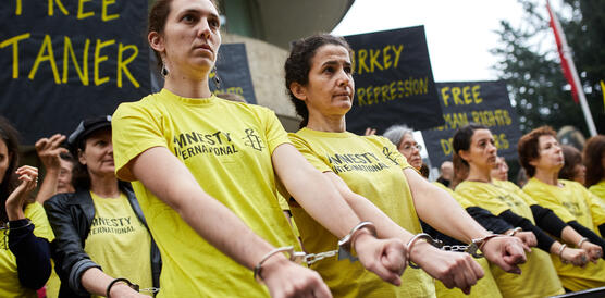 Frauen in gelben T-Shirts und in Handschellen protestieren vor einem Gebäude