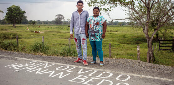 Ein Junge und ein Mädchen stehen am Rand einer Straße, vor ihnen auf dem Boden steht mit weißer Schrift "Sin olvido Hernan Bedoya"