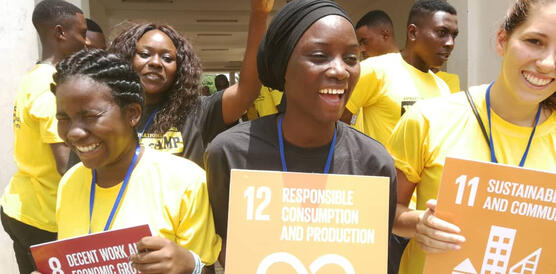 Lachende Jugendliche in gelben T-Shirts posieren mit Schildern, auf denen die "Sustainable Development Goals" der UN stehen