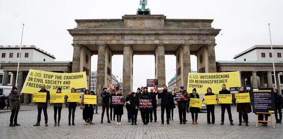 Eine Reihe schwarzgekleideter Menschen, die vor dem Brandenburger Tor Schilder und Transparente hochhalten