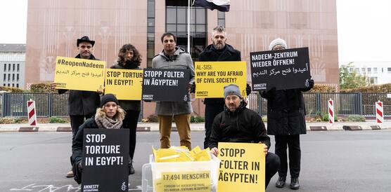 Eine Gruppe von Menschen mit gelben und schwarzen Transparenten, dahinter eine Fahne und ein Gebäude