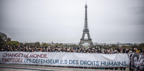 Menschenmenge mit großem Transparent in französischer Sprache, dahinter der Eifelturm.