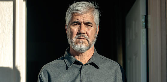 Porträtfoto eines Mannes mit Bart in grauem Hemd vor einer geöffneten Tür