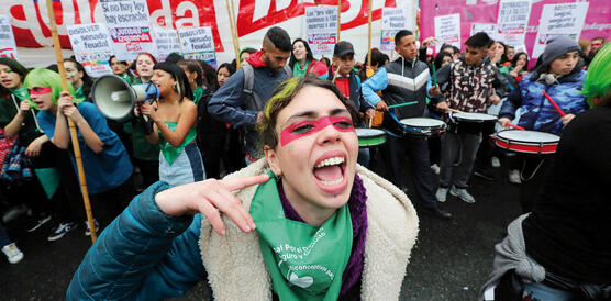 Viele Frauen und auch Männer demonstrieren mit Bannern und Plakaten, im Vordergrund ruft eine Frau