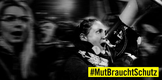 Schwarz-Weiss-Bild von einer demonstrierenden jungen Frau, die in ein Megaphon spricht. Dadrunter ein Hinweis auf den Hashtag "MutBrauchtSchutz"