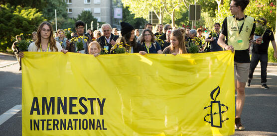 Junge Menschen tragen am Anfang eines Strassenumzugs ein großes, gelbes Amnesty-Banner und gelbe Blumen
