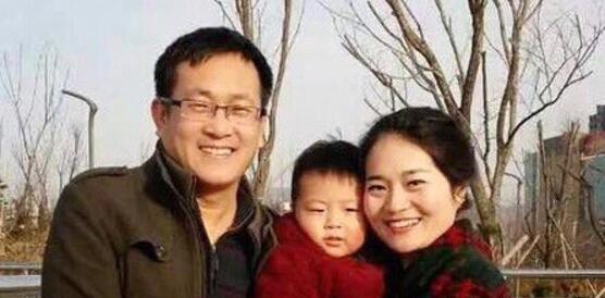 Ein junger chinesischer Mann mit Brille und eine junge chinesische Frau mit naxch hinten gekämmten Haar halten gemeinsam ein kleines Kind auf dem Arm und lächeln in die Kamera.