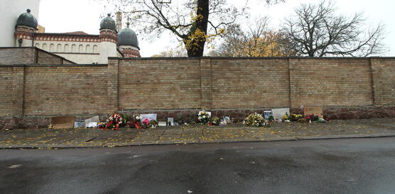 Hohe Backsteinmauer vor einer Synagoge, davor Blumen, Gedenkkarten und Kerzen