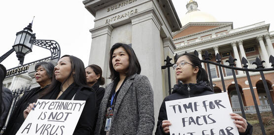 Mehrere Frauen stehen vor einem Gebäude und demonstrieren, sie halten Schilder mit der Aufschrift "Meine Ethnizität ist kein Virus" und "Zeit für Fakten, nicht für Angst"