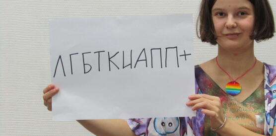 Eine junge Frau hält einen Zettel mit russischer Schrift in die Kamera.