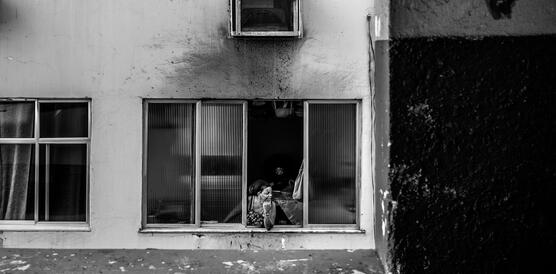 Eine Bewohnerin des Stadtviertels Cruzada São Sebastião in Rio de Janeiro, Brasilien, schaut aus einem Fenster und stützt dabei ihren Arm auf der Fensterbank auf.