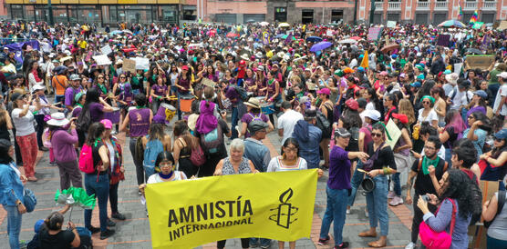 Eine Menschenmenge auf einem Platz, in der Mitte wird ein gelbes Spruchband hoch gehalten, auf dem "Amnistia" steht.