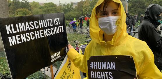 Unterstützer_in von Amnesty bei der Klimademo, in gelber Regenjacke, weil es regnet und mit Schild "Klimaschutz ist Menschenschutz"