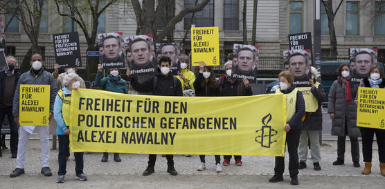 Das Bild zeigt mehrere Personen mit Amnesty-Bannern und Plakaten, im Hintergrund ein großes Gebäude