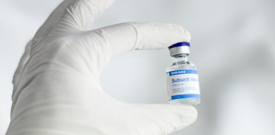 Das Bild zeigt einen Hand in einem Handschuh, mit einer Impf-Ampulle
